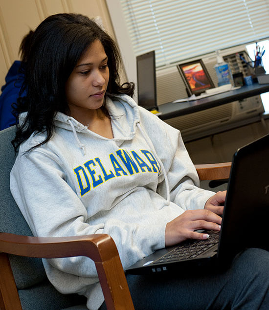 A student wearing a University of Delaware sweatshirt studies statistics on her laptop at home.